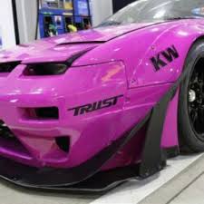 front side of a pink car with slightly closed headlights and a few decals on it